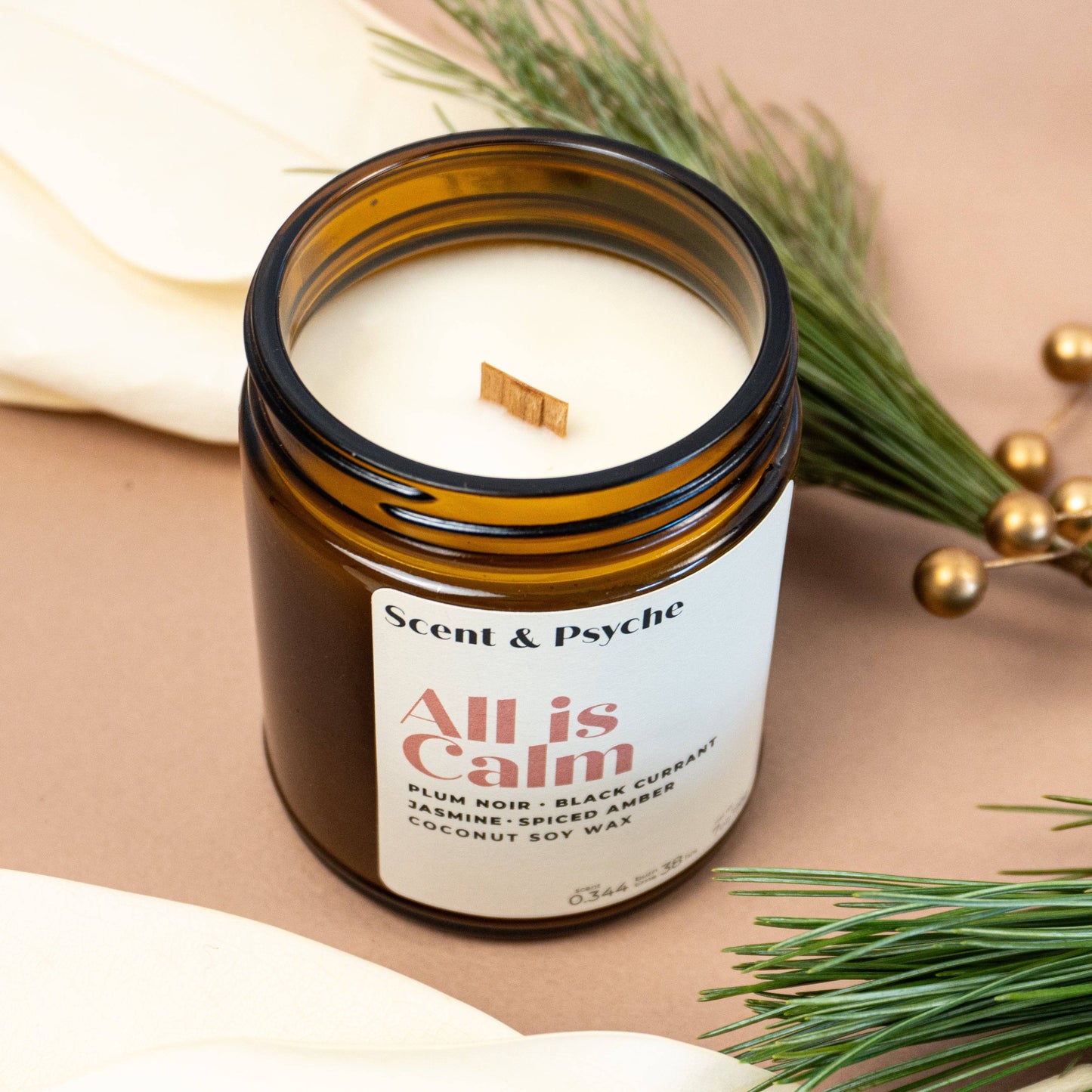 Open All is Calm Scented Candle in 7oz amber jar with wooden wick, made from coconut soy wax. Perfect for cozy seasonal ambiance and gifting.