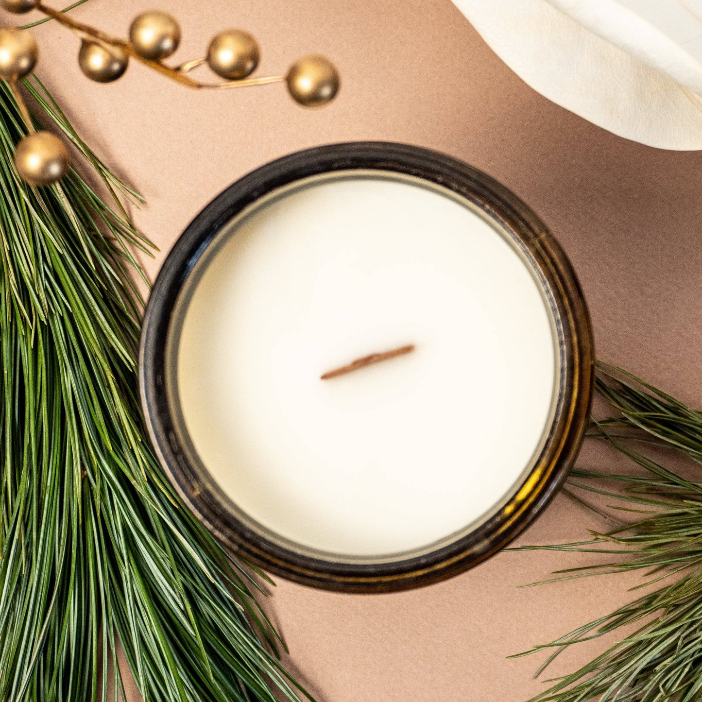 Top view of All is Calm Scented Candle - 15oz with wooden wick and creamy coconut soy wax, styled with pine and gold holiday accents.