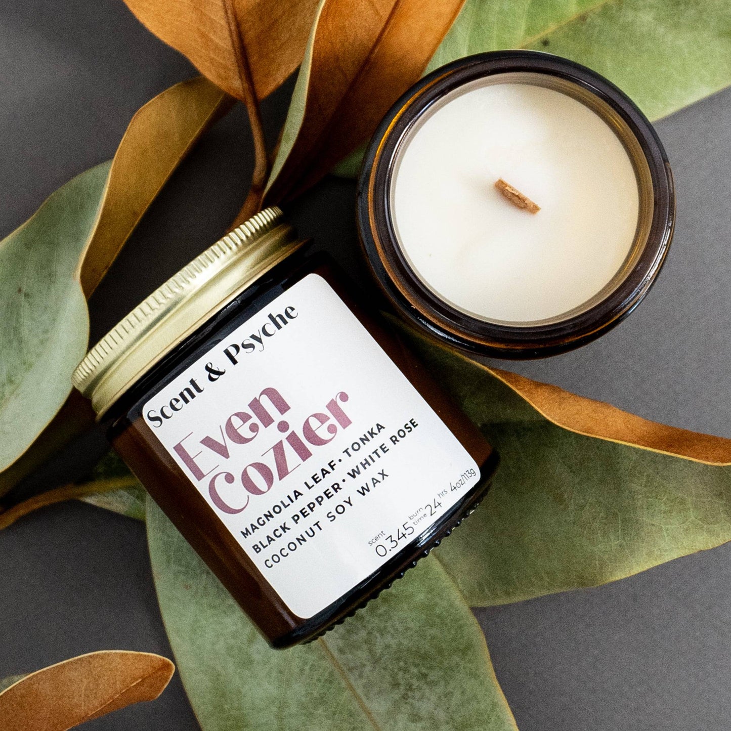 Scented Candle 4oz - Even Cozier Wood Wick Candle in amber jar with lid off, displayed on autumn leaves. Clean-burning coconut soy wax.