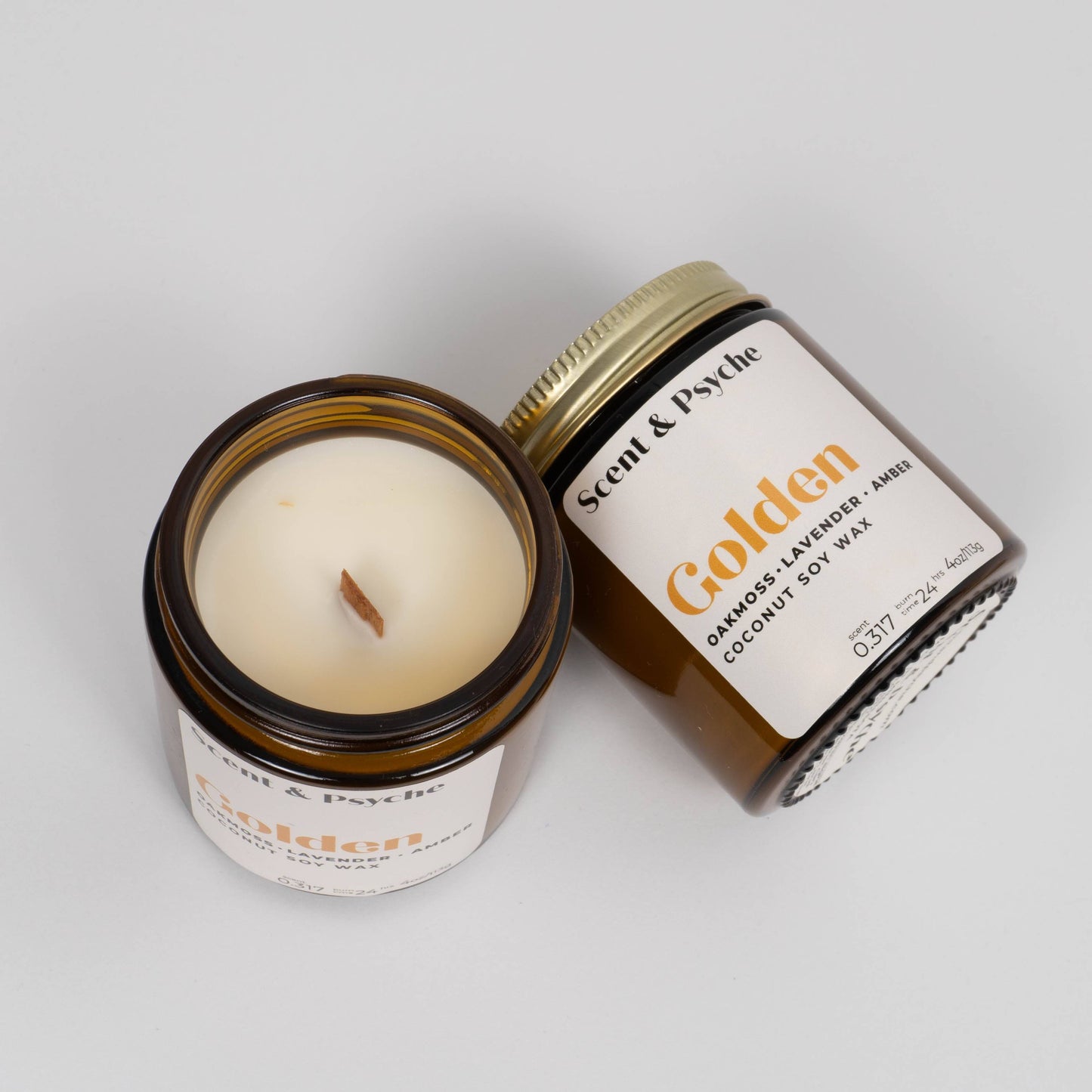 Golden Scented Candle in a 4oz amber jar, one standing upright and another open showing the wooden wick. Infused with oakmoss, lavender, and amber scents.