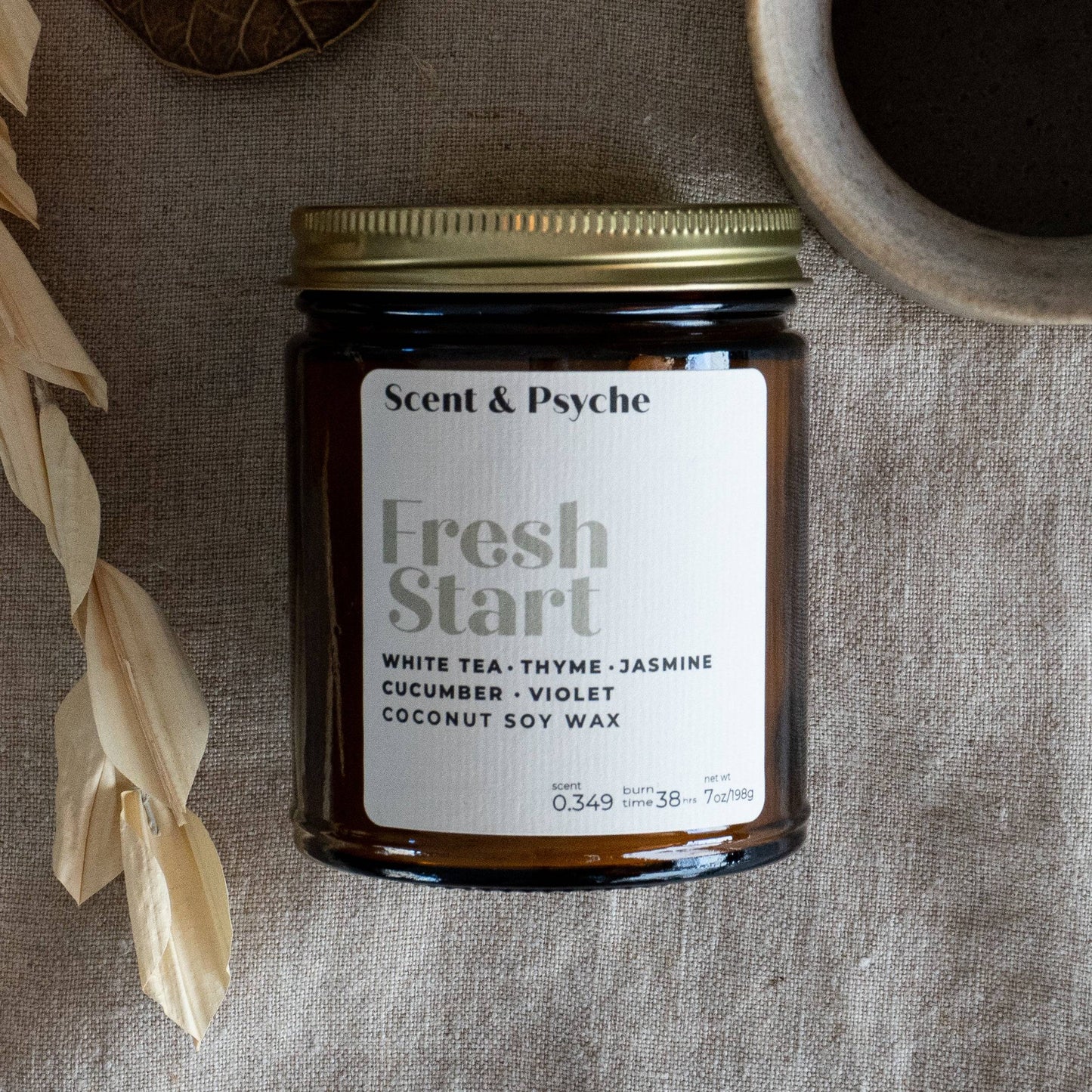 Fresh Start Wood Wick Scented Candle in a 7oz amber jar with a gold lid. Features a blend of white tea, thyme, jasmine, cucumber, and violet.