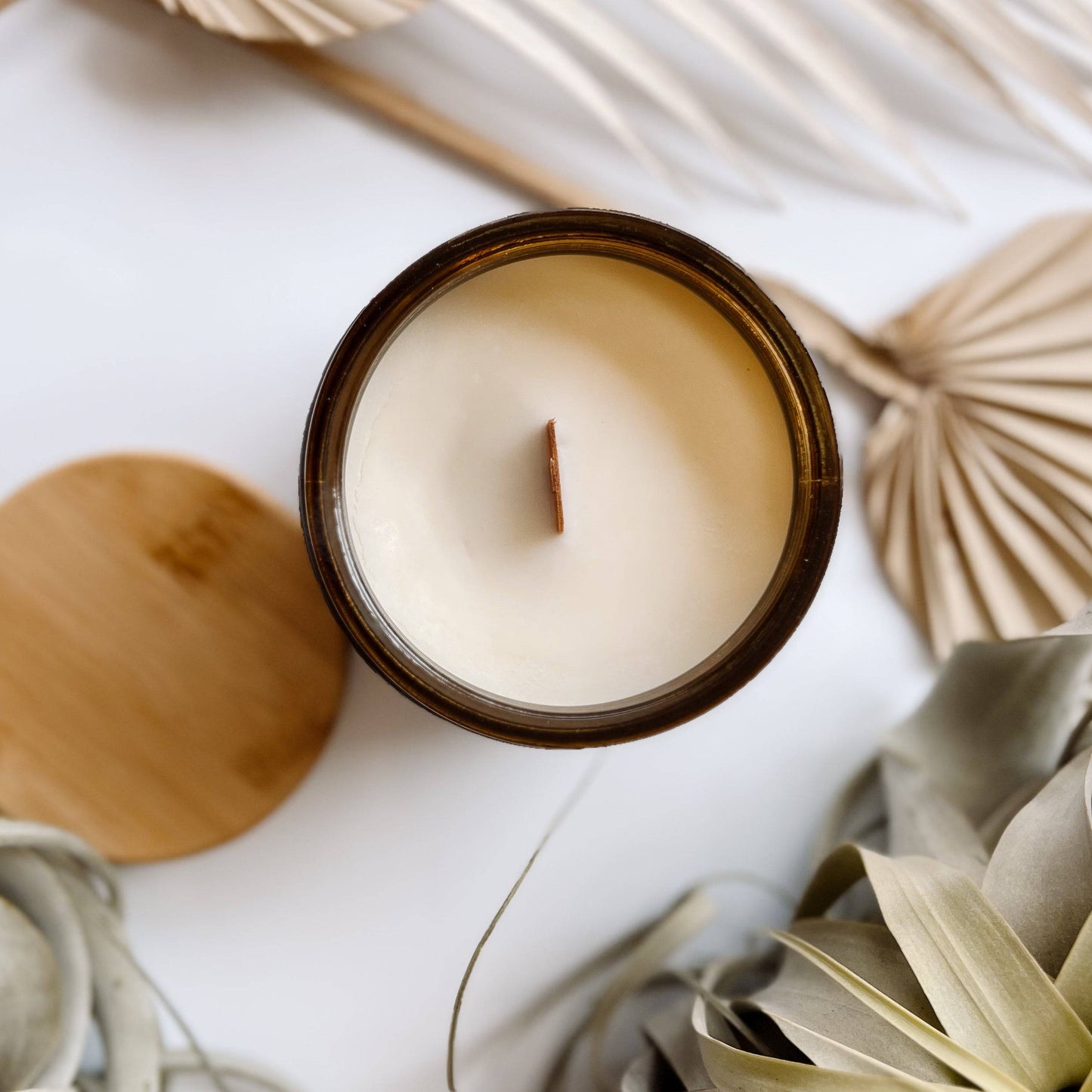 Top view of the Casita Scented Candle in a 12oz amber jar, showcasing a wooden wick and smooth coconut soy wax, surrounded by dried botanical decor.