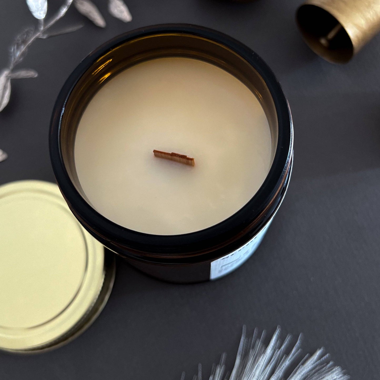 Noel Wood Wick Scented Candle in a 7oz amber jar with an open lid, revealing a smooth coconut soy wax surface and a wooden wick for a cozy burn.