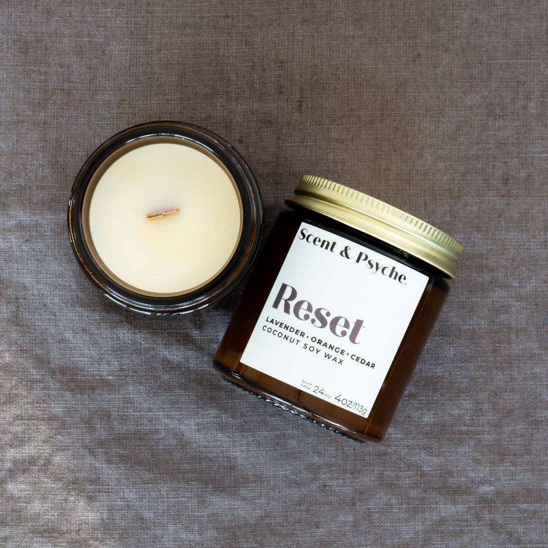 Reset Wood Wick Scented Candle in a 4oz amber jar with a gold lid, featuring a blend of lavender, orange, cedar, and coconut soy wax. Perfect for relaxation and renewal.