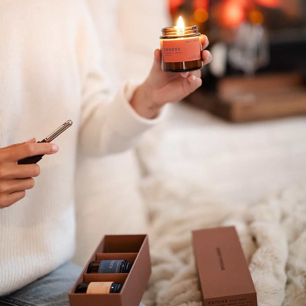 Person in cozy sweater holding open Scent + Psyche Discovery Bundle with lit candle — fall candle gift set