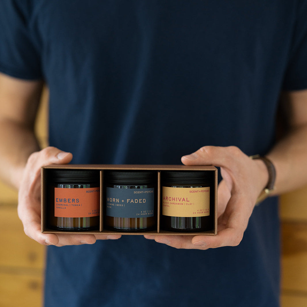 Hands holding open Scent + Psyche Discovery Bundle gift box with Embers, Worn + Faded, and Archival wood wick candles