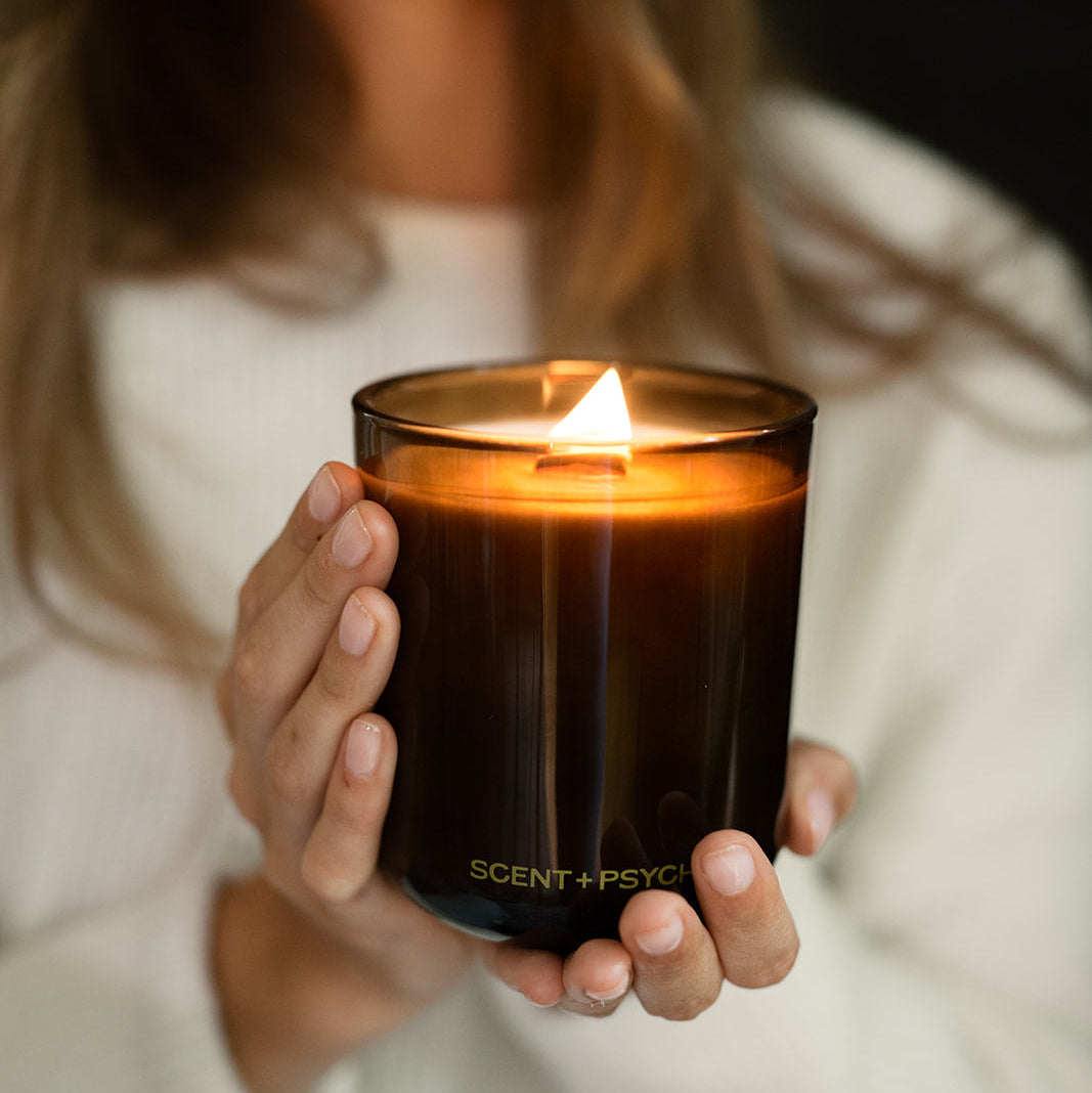 Woman smiling while holding a lit Statement Size Scent + Psyche candle in both hands