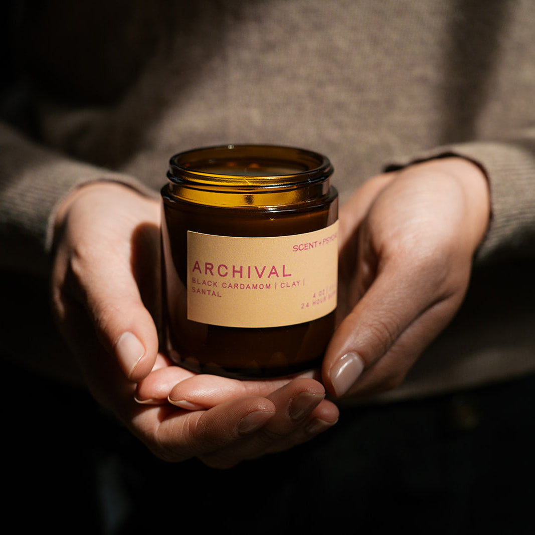 Person holding a 'Archival' candle in their hands with a dark background