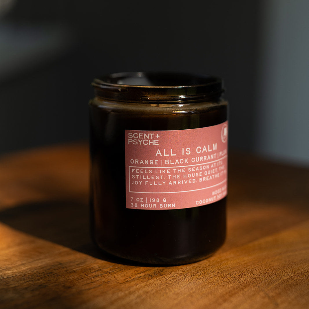 All is Calm wood wick candle on a wooden surface with a dark background