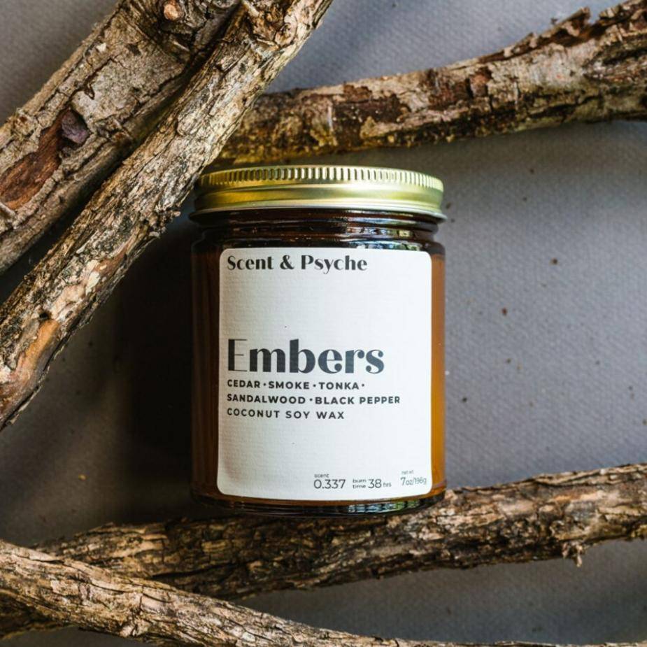 Embers Scented Candle in a 7oz amber jar with a gold lid, featuring notes of cedar, smoke, tonka, sandalwood, black pepper, and coconut soy wax.