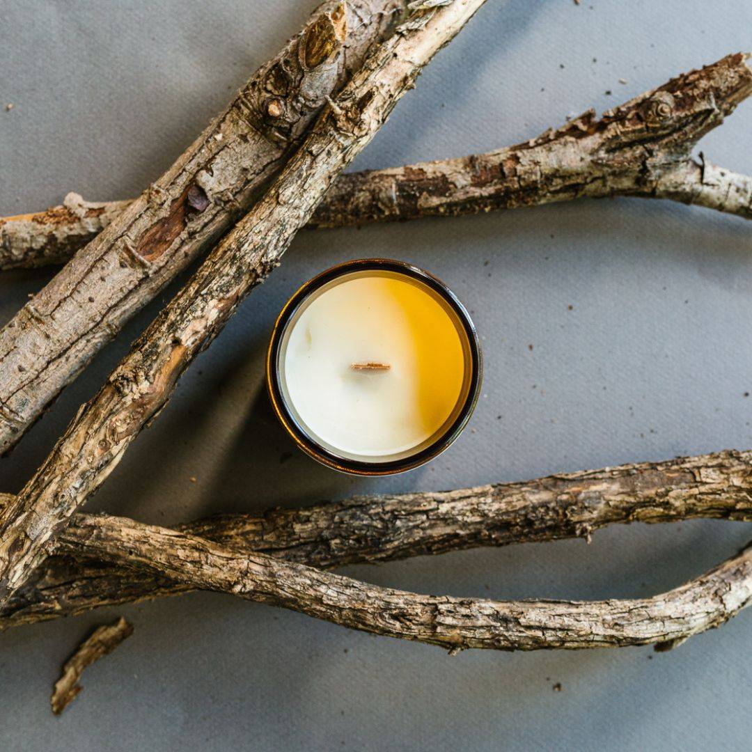 Top view of Embers Scented Candle in a 7oz amber jar with a wooden wick, surrounded by rustic branches, evoking a warm and cozy ambiance.