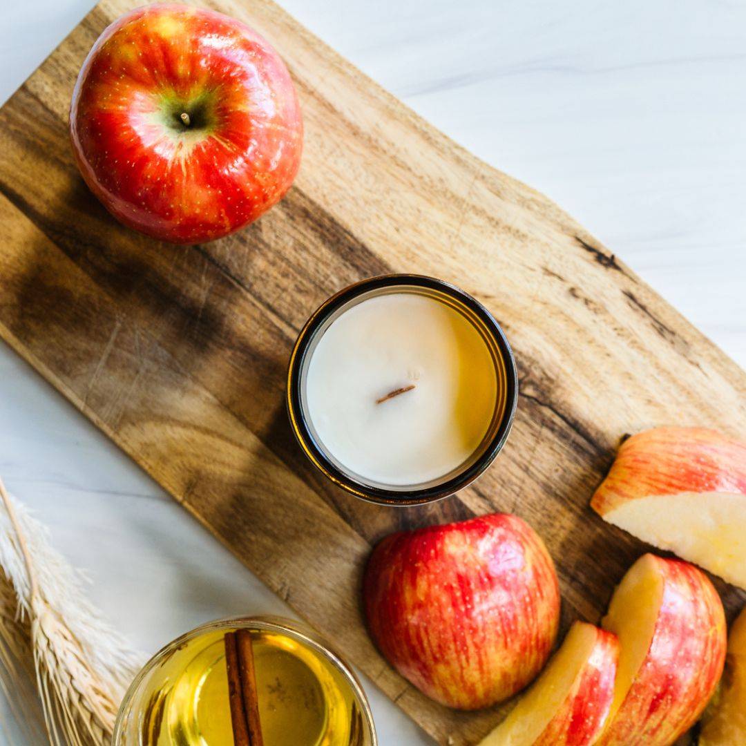 Top view of the Cider House 7oz amber jar candle with a wooden wick, surrounded by fresh apples and cider. A cozy fall fragrance for home ambiance.