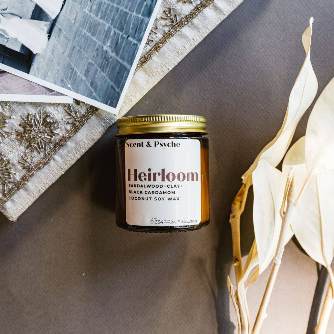 Heirloom Scented Candle in a 4oz amber jar with a gold lid, featuring sandalwood, clay, and black cardamom fragrance. Perfect for home ambiance.