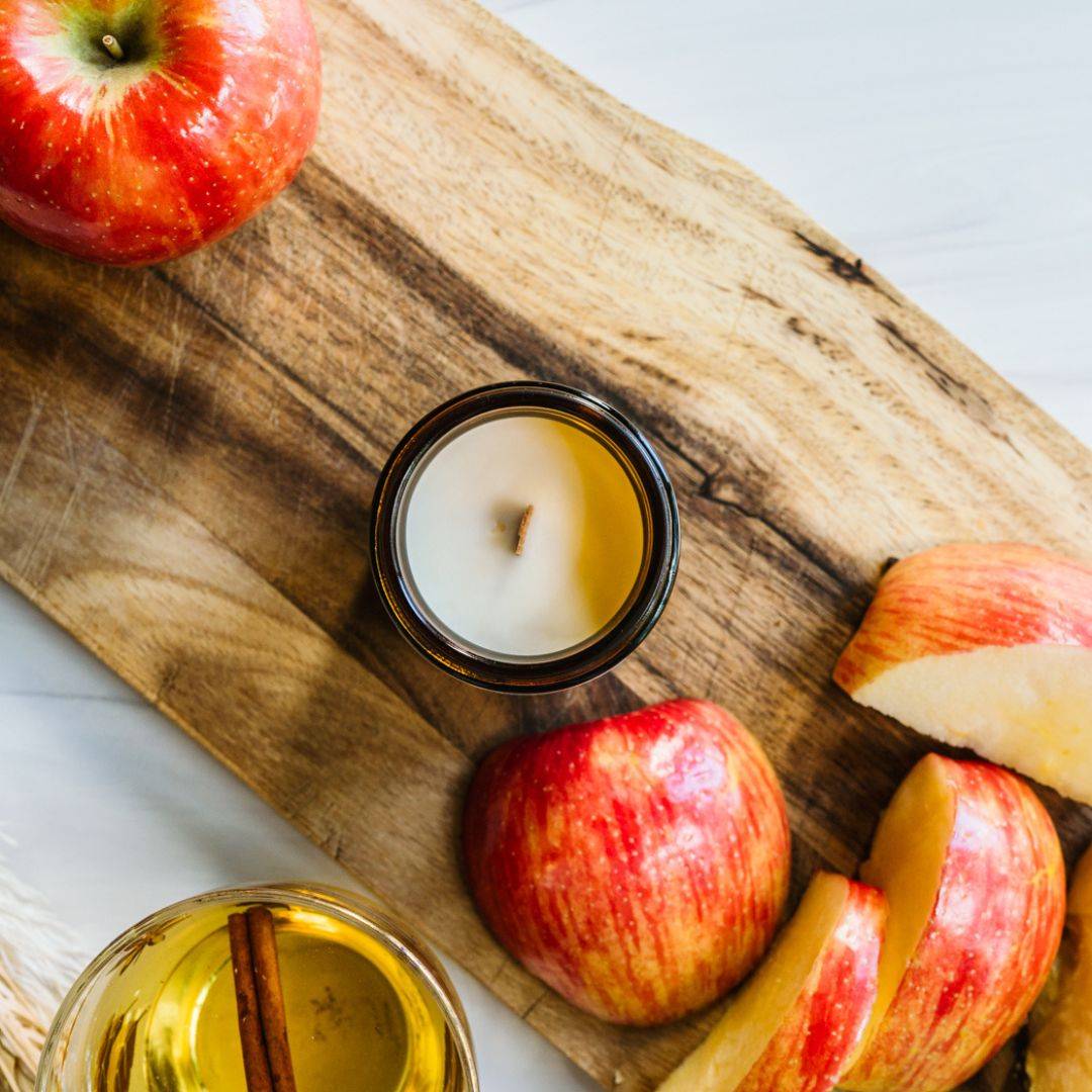 Top view of the Cider House Scented Candle in a 4oz amber jar, surrounded by fresh apples and a cinnamon-infused drink, evoking warm autumn vibes.