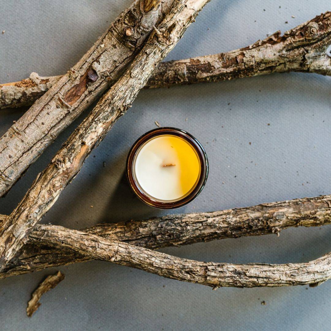 Top view of Embers Scented Candle in a 4oz amber jar, showcasing a smooth coconut soy wax surface, surrounded by natural wooden branches.