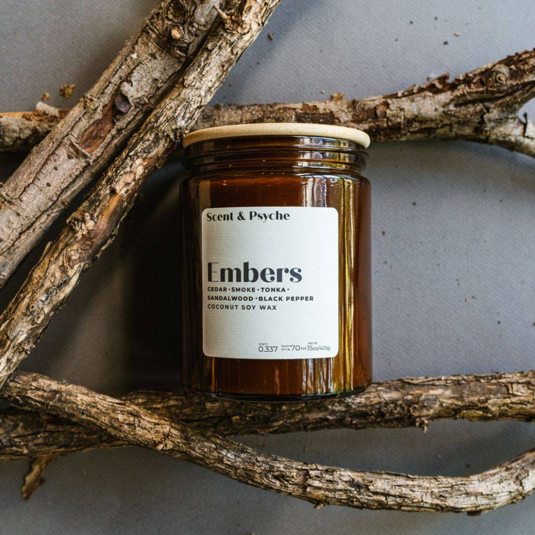 Embers Scented Candle in a 15oz amber jar with a wooden lid, featuring notes of cedar, smoke, tonka, sandalwood, and black pepper. Perfect for fall ambiance.