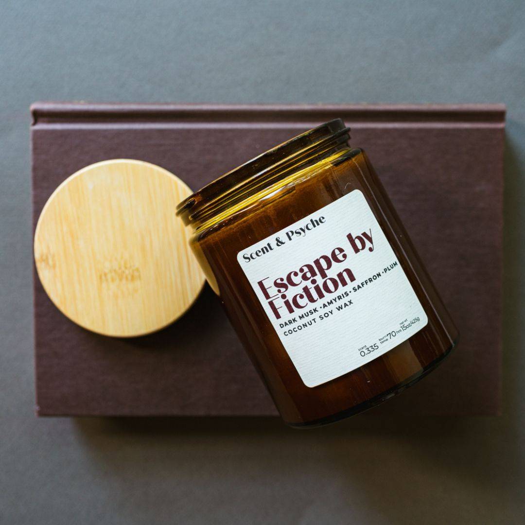 Escape by Fiction Scented Candle in a 15oz amber jar with a wooden lid. Features dark musk, nutmeg, saffron, and plum scents for a cozy ambiance.