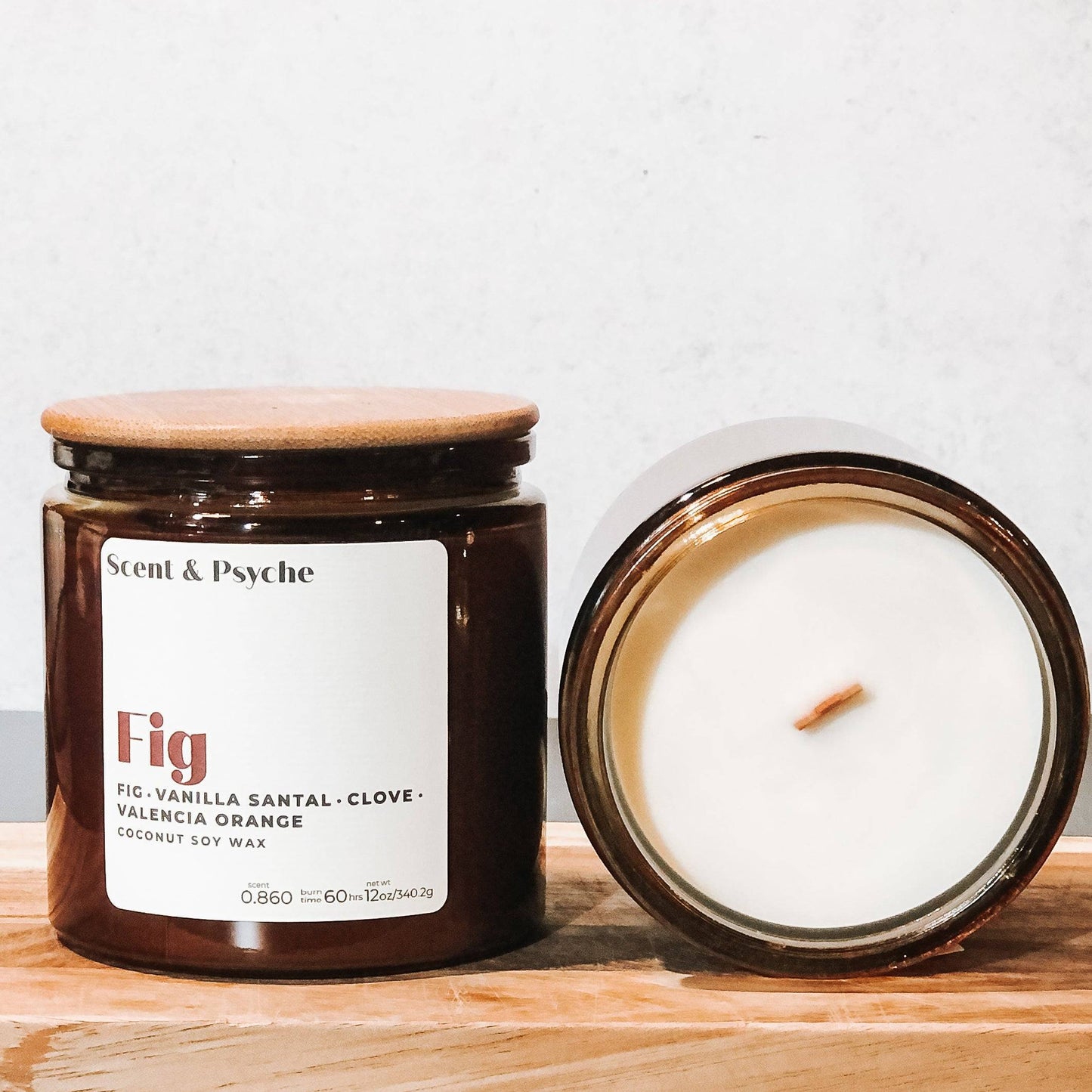 Fig Scented Candle in a 12oz amber jar with a wooden lid, displayed with an open candle showing a wooden wick. A premium coconut soy wax candle.