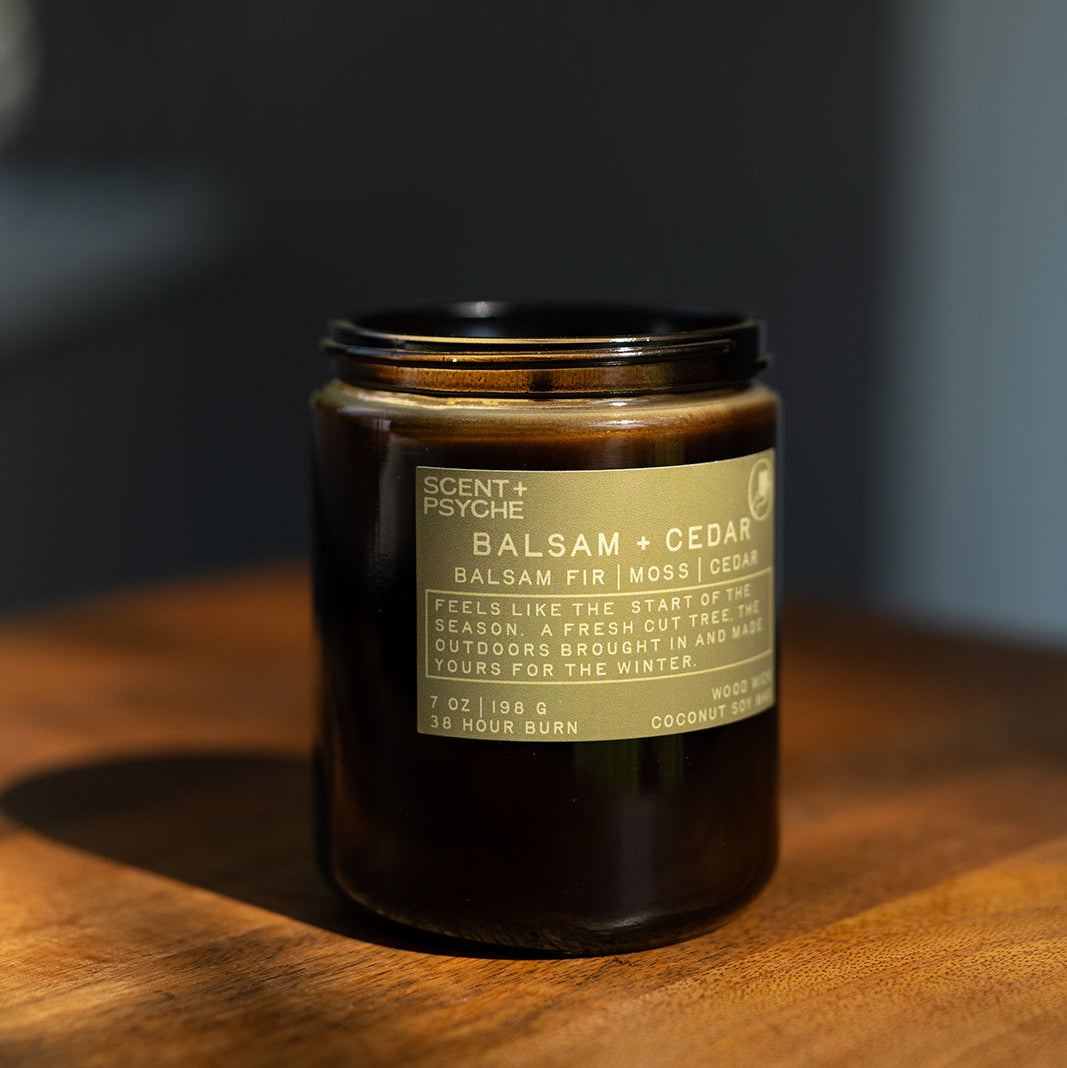 Balsam + Cedar wood wick candle on a wooden surface with a dark gray background