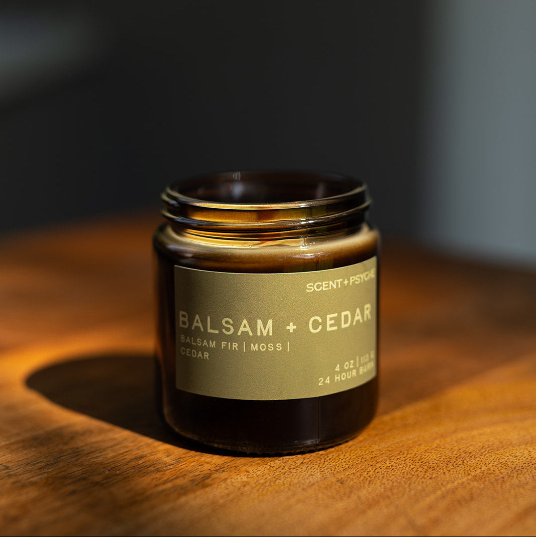 Balsam + Cedar candle on a wooden surface in warm light with a dark background