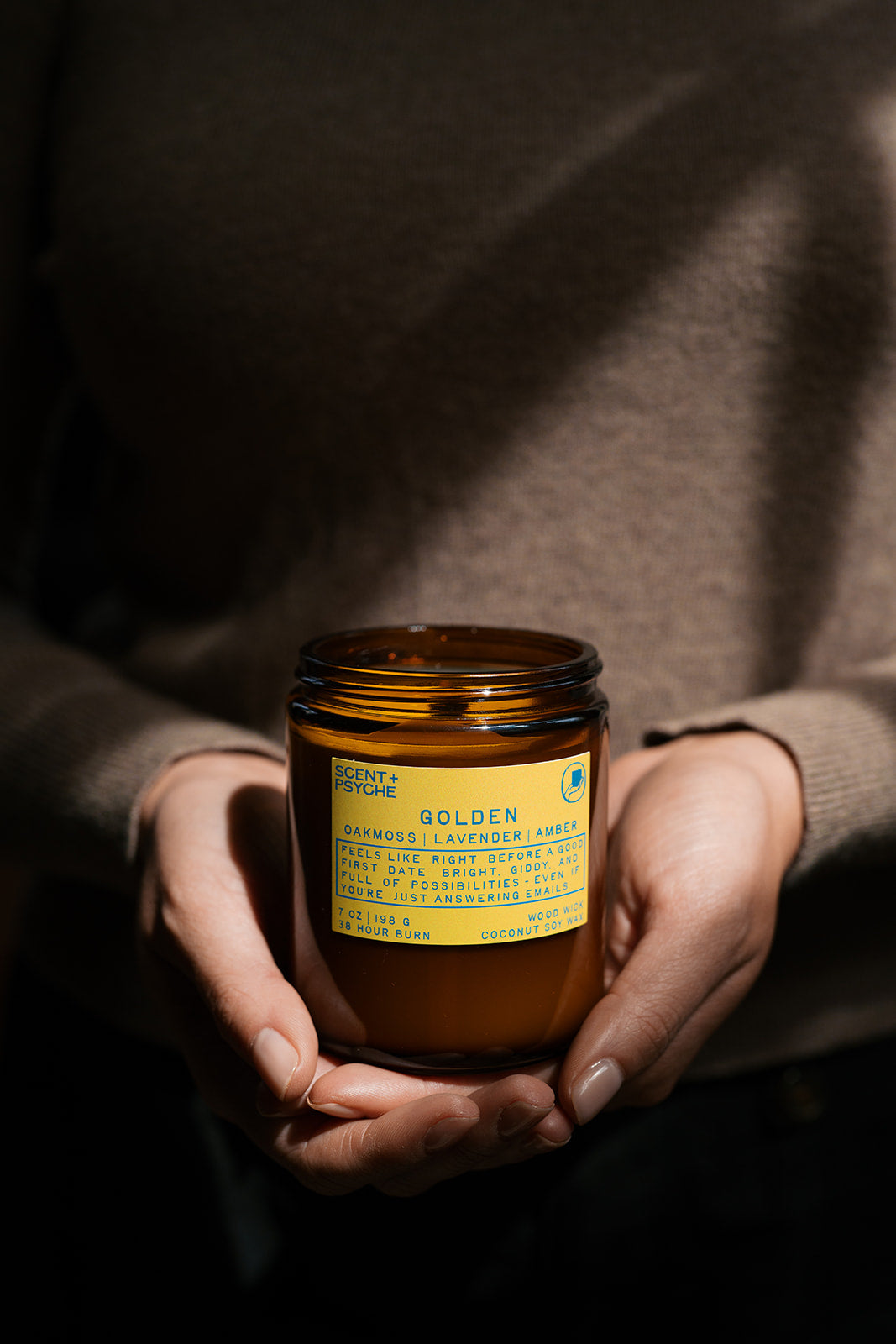Energizing + Fresh Scented Candle Bundle | Signature Size.  Golden Candle Person holding a jar of 'Golden' candle with a label, against a dark background