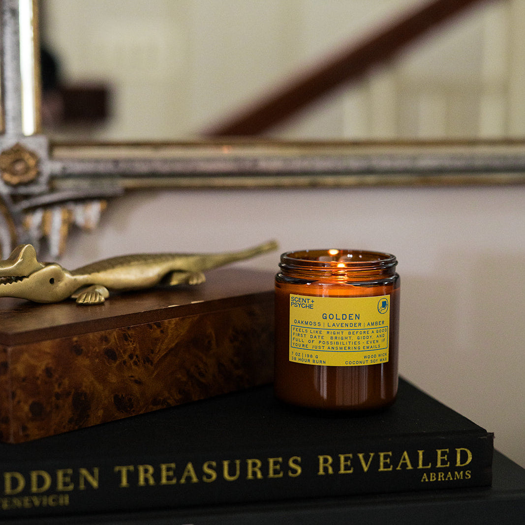 Golden wood wick candle  on top of books with decorative elements in the background