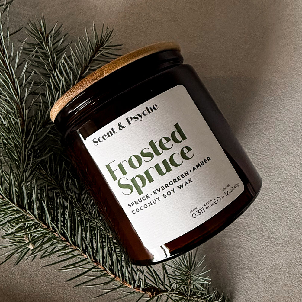 Candle jar labeled 'Frosted Spruce' by Scent & Psyche with a wooden lid on a neutral background.