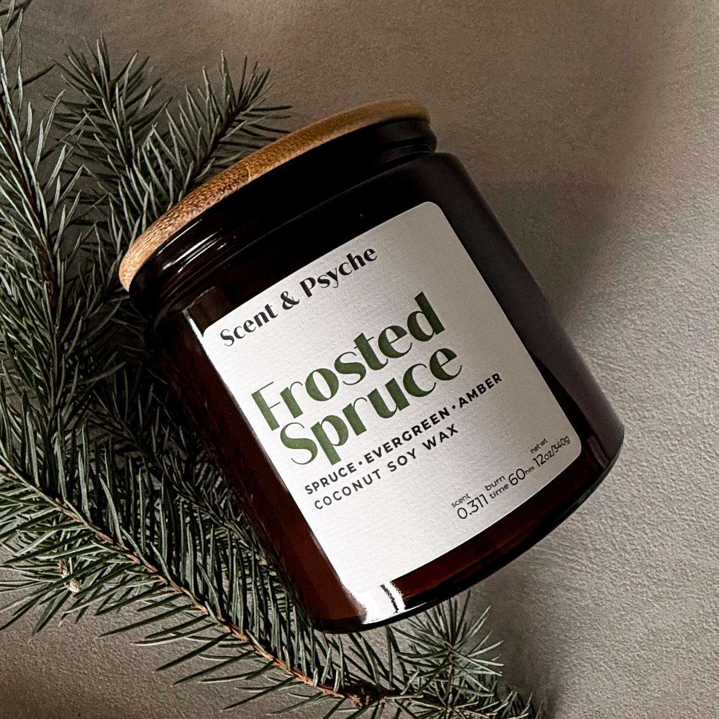 Candle jar labeled 'Frosted Spruce' by Scent & Psyche with a wooden lid on a neutral background.