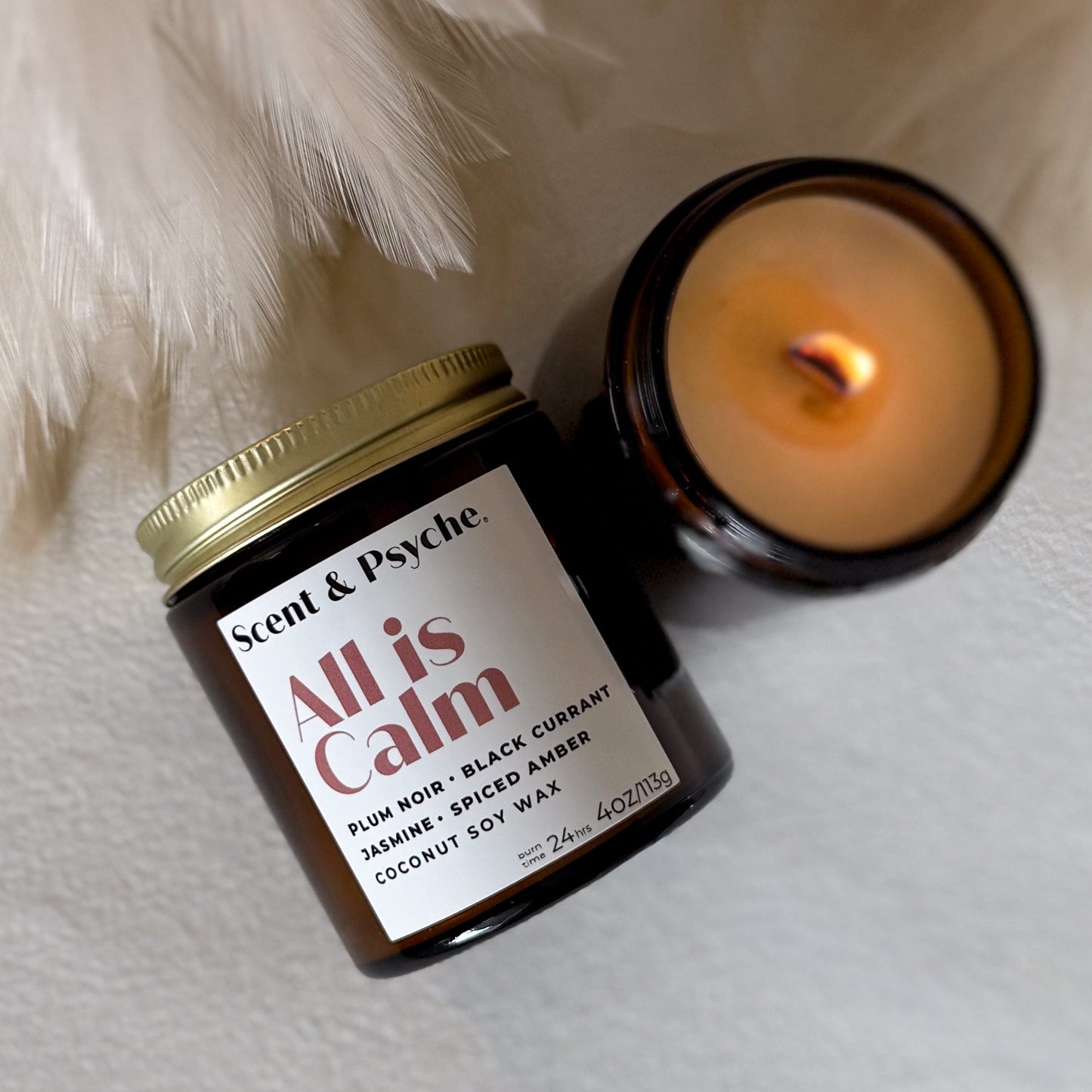 Candle and jar labeled 'All is Calm' by Scent & Psyche on a soft surface.