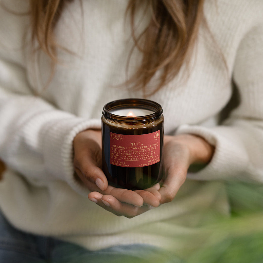Woman in a cream sweater holding a Noel candle in both hands
