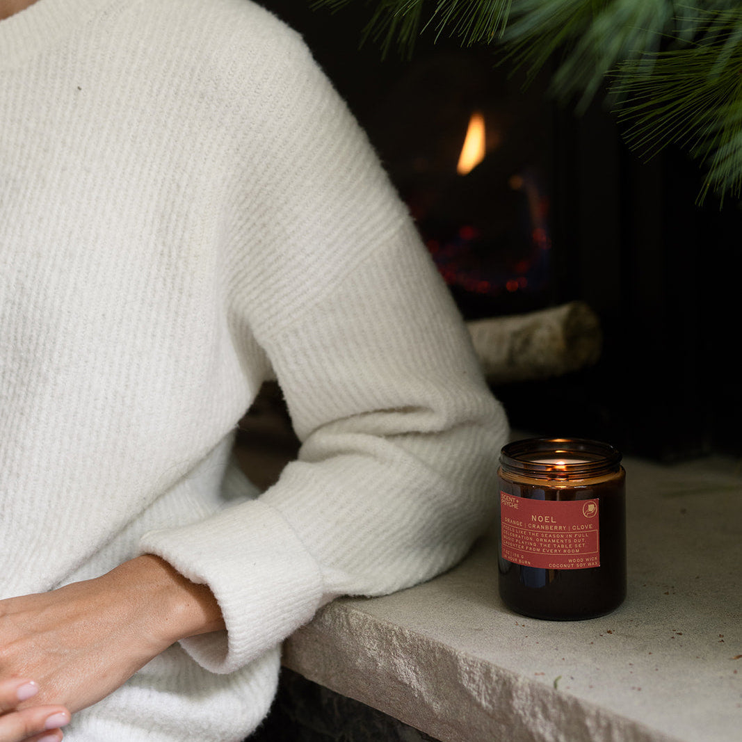 Noel candle on a fireplace hearth with pine branches, woman relaxing by the fire