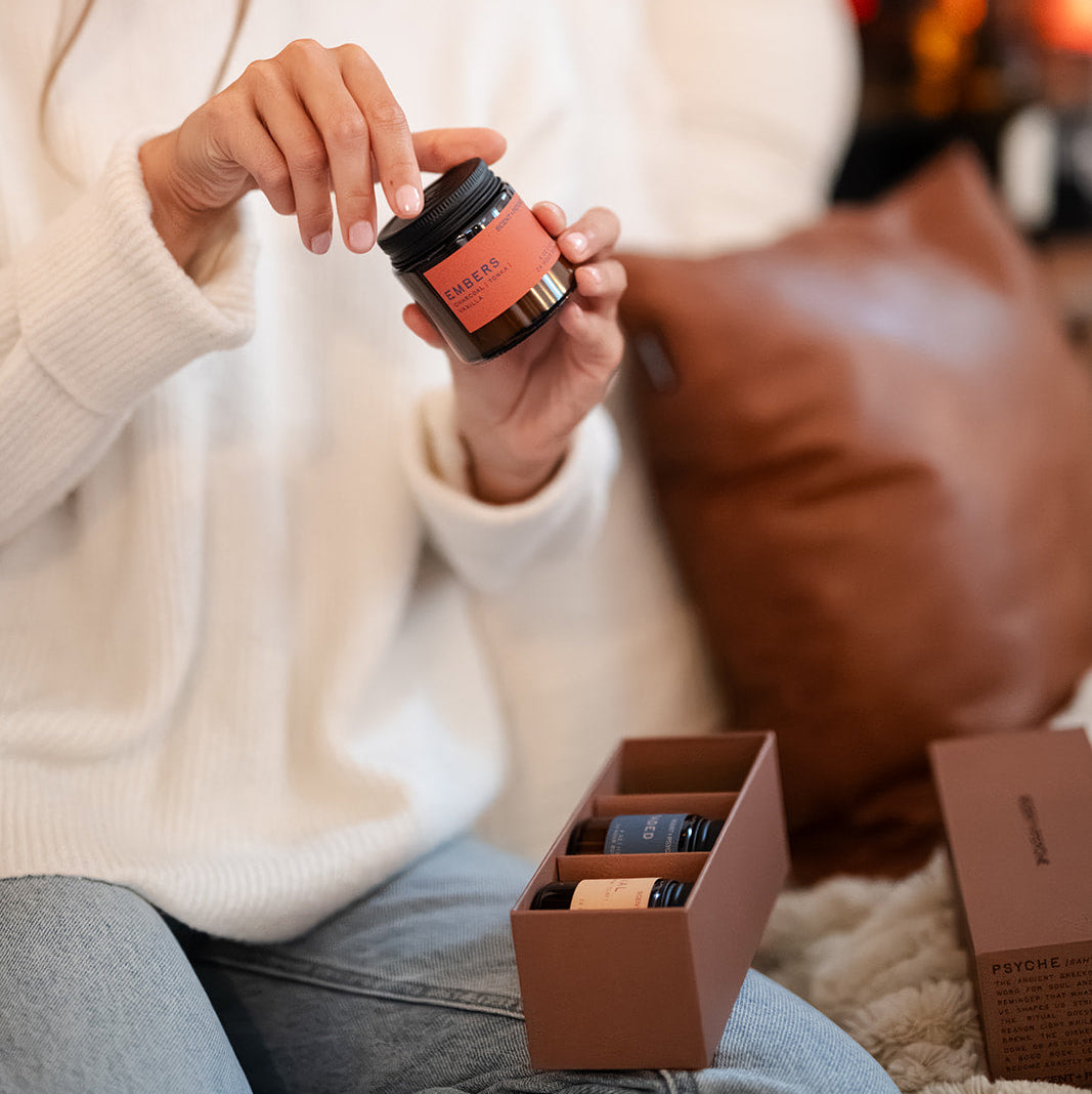 Close-up of hand holding Embers wood wick candle from Scent + Psyche Warm + Cozy Discovery Bundle — charcoal tonka santal