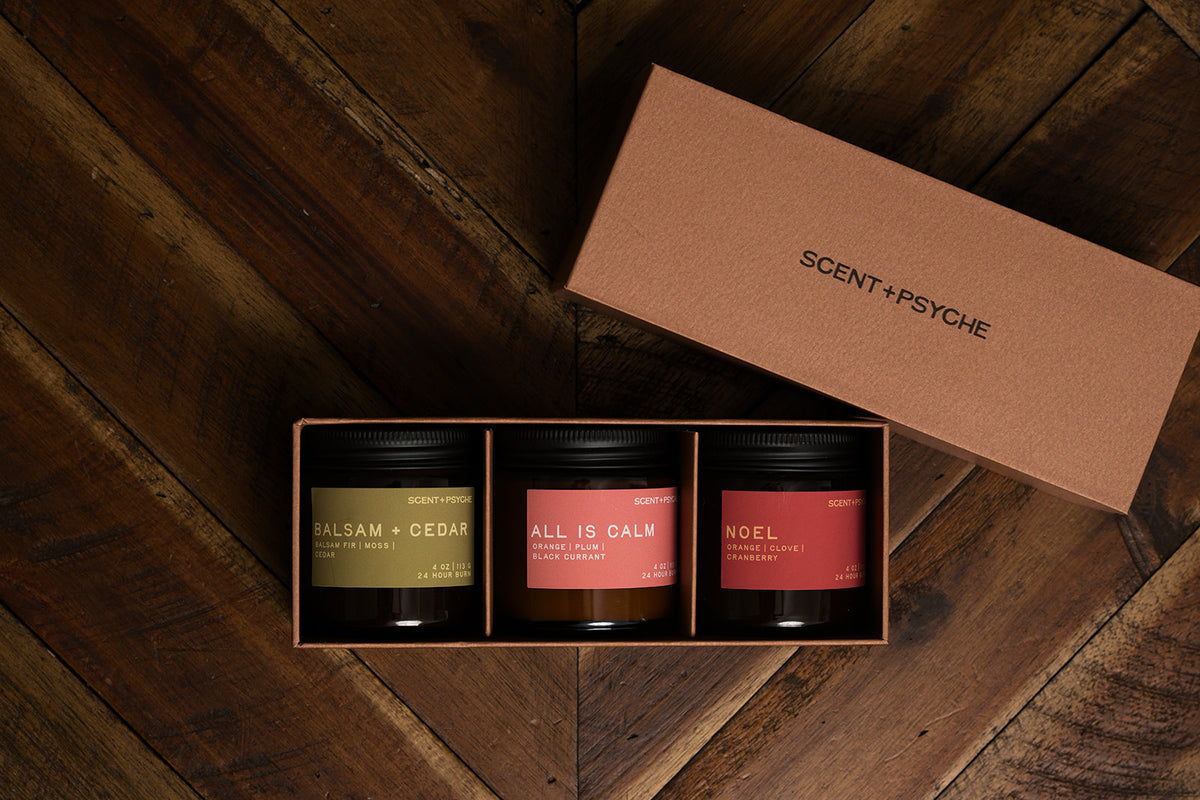 Holiday Discovery candle gift set: Balsam + Cedar, All is Calm and Noel 4 oz candles in a Scent + Psyche gift box on a wood floor