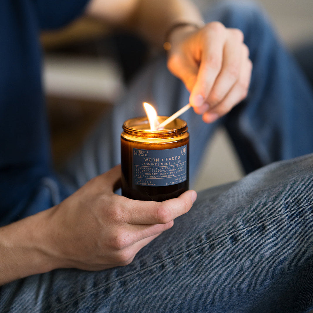 Hand holding a lit wood wick soy candle, Worn and Faded jasmine musk scent — Scent & Psyche