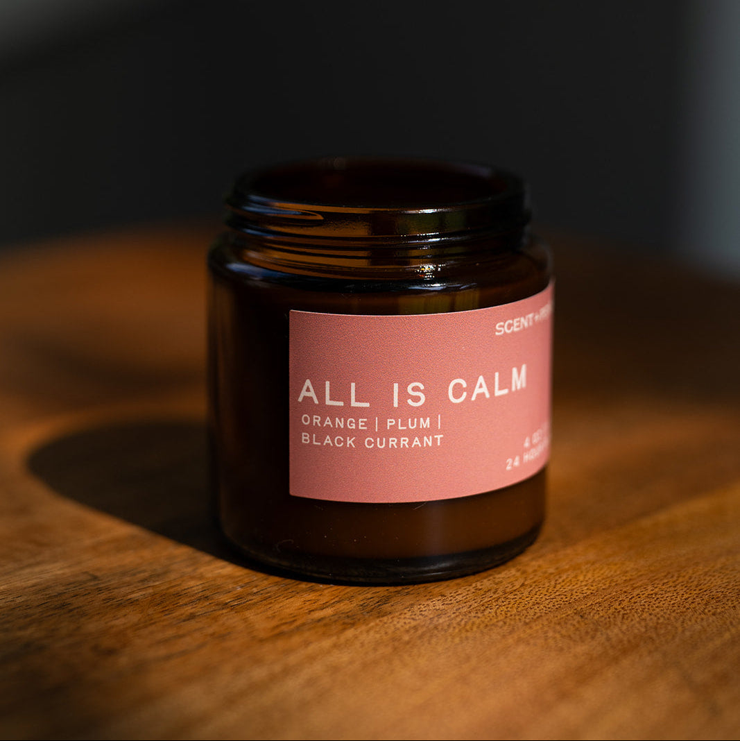 All is Calm candle on a wooden table in soft evening light