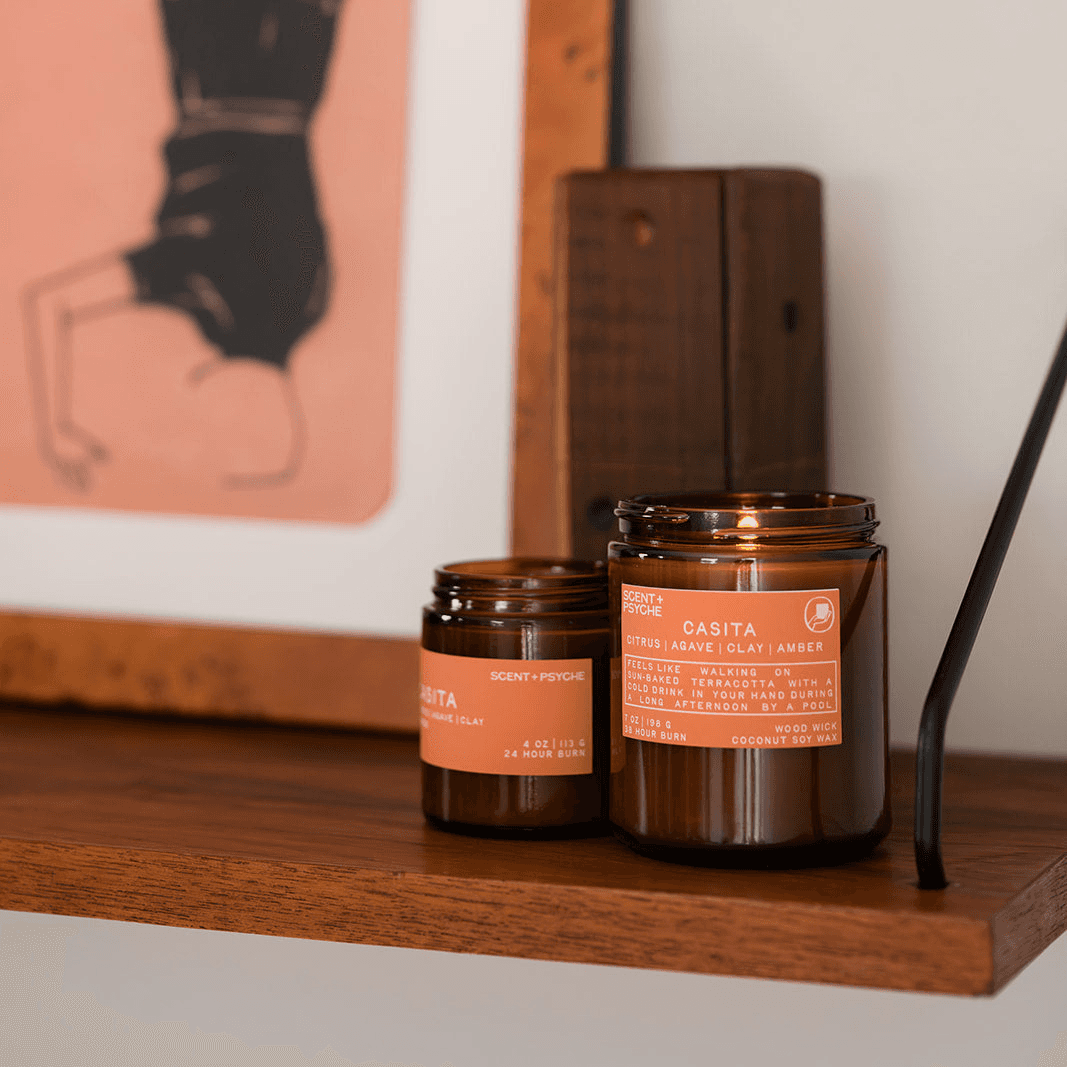 Two amber-colored candles with orange labels on a wooden shelf.