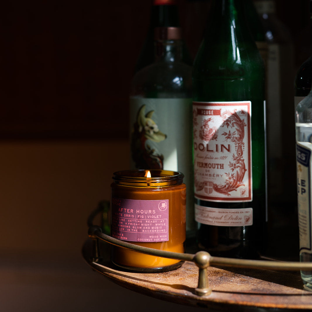 bottles and a lit candle on a wooden tray in a dimly lit setting