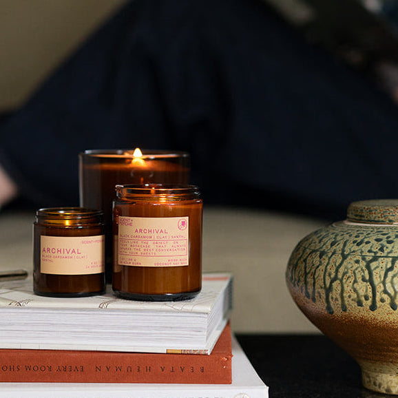 Candles and books on a table with a blurred person reading in the background