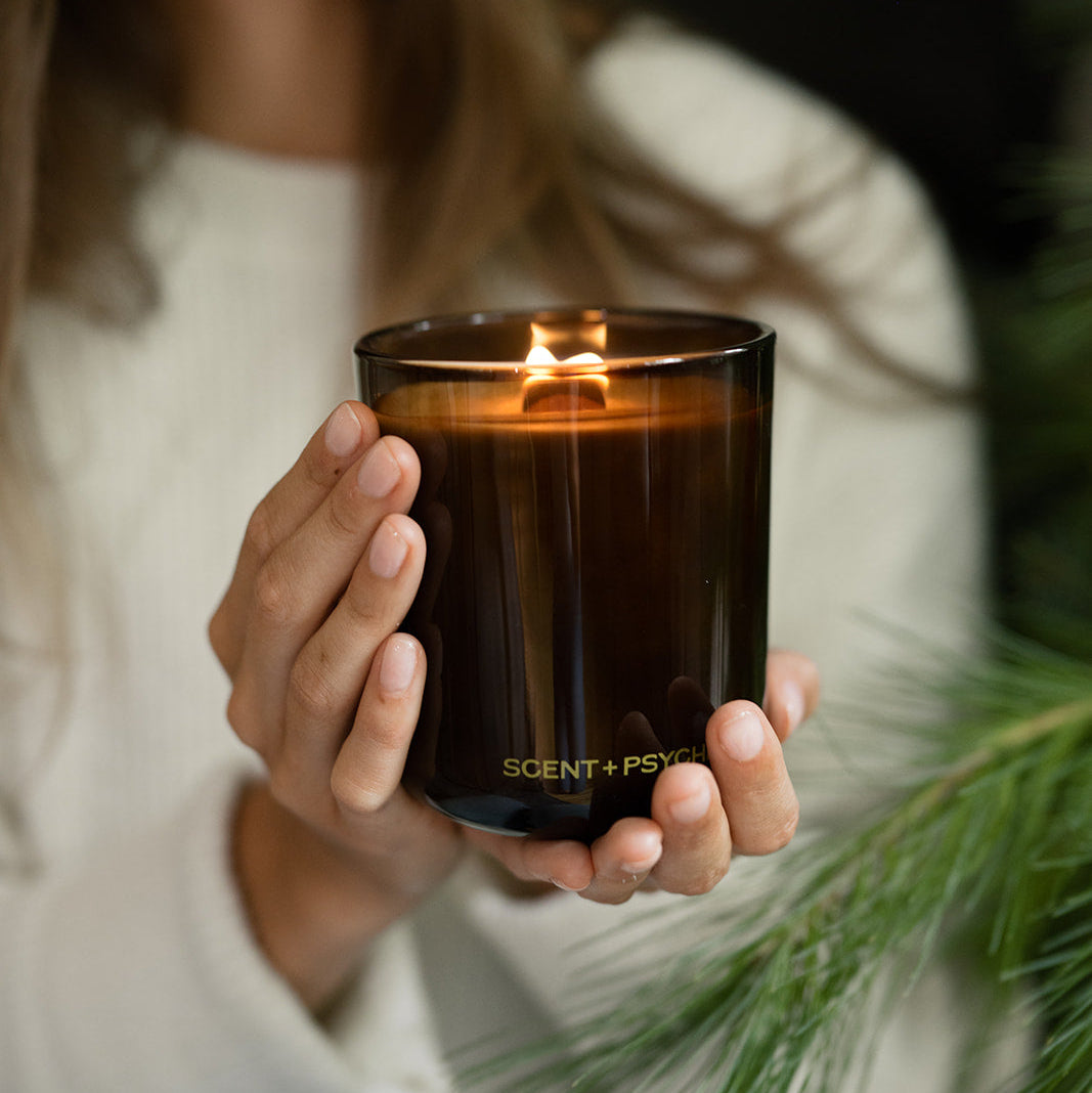 Woman in a white sweater holding a lit Scent + Psyche wood wick candle